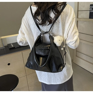 Detail of black glossy tote bag featuring a cute white pom-pom charm and bow accent