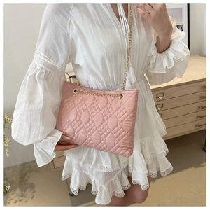 Detail of pink quilted tote bag with gold chain strap worn by a model in a dress