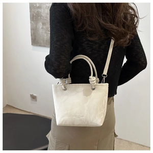 Détail d'un sac bandoulière crème avec poignées nouées et logo imprimé fashion