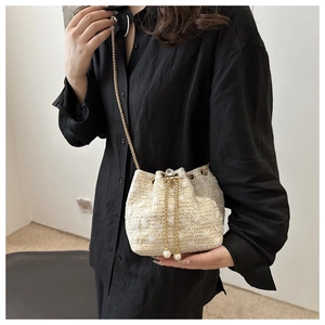 Detail of cream woven bucket bag with star patterns, gold chain, and pearl accents