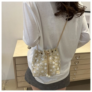 Close-up of woven bucket bag featuring floral embroidery, gold chain, and pearl charms