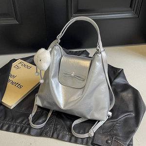 Silver metallic bow backpack with plush pendant on a black leather background