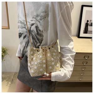 Detail of straw bucket bag with floral embroidery, pearl charms and gold chain strap