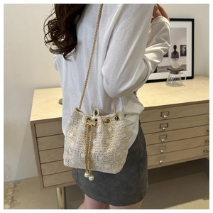 Close-up of woven bucket bag with floral embroidery, chain strap and pearl drawstring