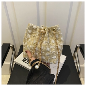Detail of straw bucket bag featuring white daisy embroidery and pearl drawstring charms
