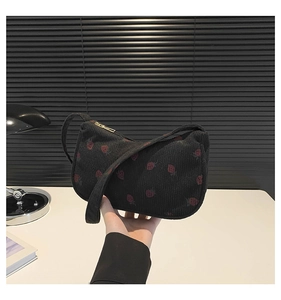 Détail de broderie fraise sur sac sous le bras en velours côtelé noir avec zip doré