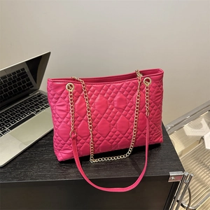 Rose red quilted tote bag with gold chain strap placed on a wooden desk near a laptop