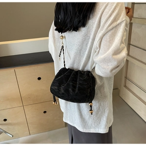 Detail of black pleated cloud bag with golden ball woven chain strap on a model