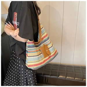 Detail of a colorful striped straw tote bag with brown leather straps worn by a model