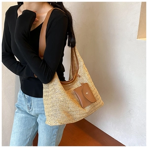 Detail of a large woven straw tote bag with brown leather trim and matching coin purse charm