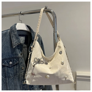 Close-up of cream textured tote bag featuring rhinestone bow, pearls and heart charms