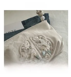 Close-up of elegant floral embroidery and pearl handle on beige silk shoulder bag