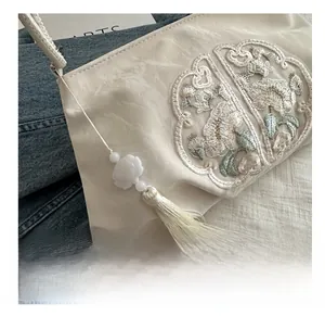Close-up of floral embroidery and long tassel charm on a cream pleated crossbody bag