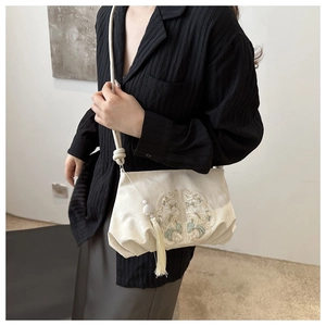 Detail of floral embroidery and fringe tassel on cream faux leather crossbody bag