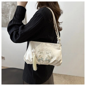 Detail of white silk handbag with green floral embroidery and elegant long tassel