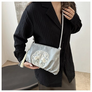 Detail of grey crossbody bag with traditional Chinese floral embroidery and white tassel