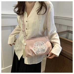 Detail of pink crossbody bag featuring white floral embroidery and tassel charm