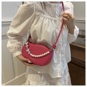 Pink crescent crossbody bag with decorative pearl and silver heart chain on white lace top