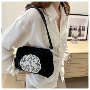 Detail of black velvet crossbody bag with white floral embroidery and long tassel
