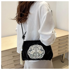 Detail of black velvet crossbody bag with white floral embroidery and tassel on model