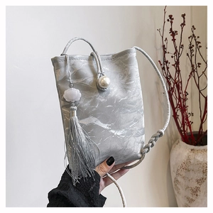 Detail van zilveren zijden crossbodytas met parelsluiting en elegante kwastjeshanger
