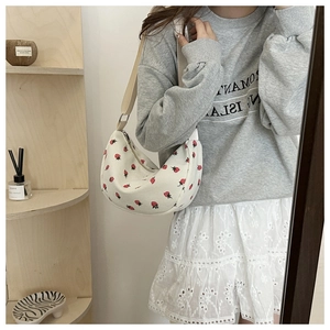 Detail of white crossbody crescent bag with red strawberry print and adjustable strap