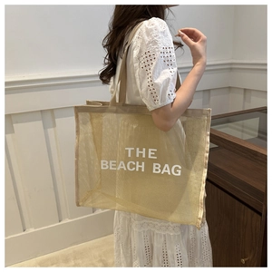 Detail of the beach bag lettering on a beige mesh tote with a minimalist design