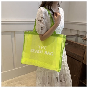 Model wearing a large neon green mesh beach tote bag with THE BEACH BAG text print
