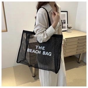 Detail view of a large black mesh tote bag featuring bold white THE BEACH BAG lettering print