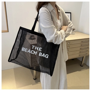 Detail of a large black mesh beach bag with white text held by a model in a warm setting
