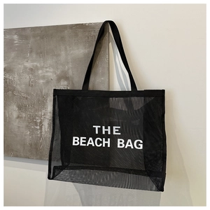 Macro detail of black mesh beach bag featuring THE BEACH BAG text and woven handles