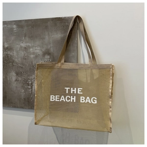 Detail of beige mesh beach tote with bold white THE BEACH BAG text and woven handles