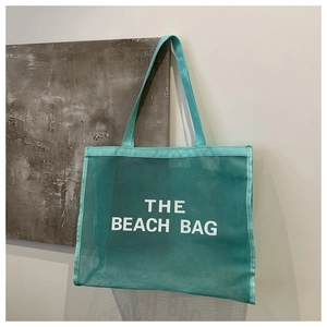 Detail of teal mesh beach bag showing breathable texture and bold white THE BEACH BAG text