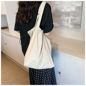Detail of off-white drawstring tote bag with black toggle worn on shoulder by a model