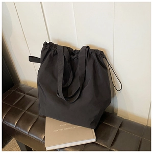 Detail of a large black drawstring tote bag made of durable nylon material on a bench