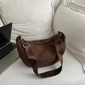 Brown corduroy strawberry print crescent shoulder bag with adjustable strap on white sofa