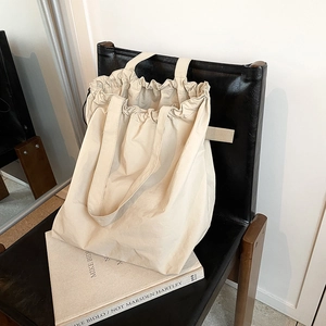 Large cream canvas tote bag with drawstring design and wide strap for daily commute