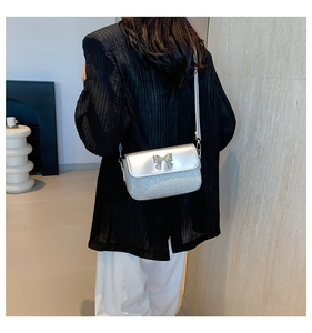 Detail of silver flap bag with a glitter finish and bow metal piece on elegant outfit