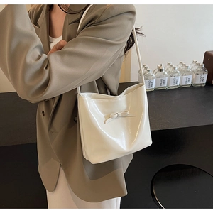 Detail of a creamy white glossy underarm bag with a delicate bow and slim strap