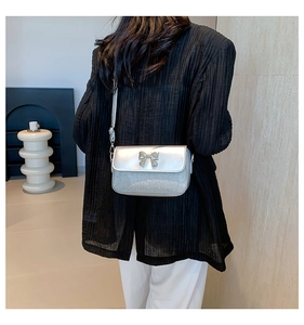 Detail of silver crossbody bag with diamond bow buckle and shimmering glitter texture