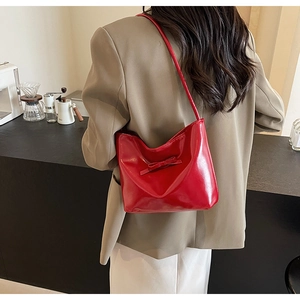 Detail of red glossy crescent shoulder bag with bow, worn by model in cafe setting