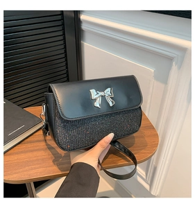 Detail of elegant black leather flap bag with silver sequins and metallic bow charm