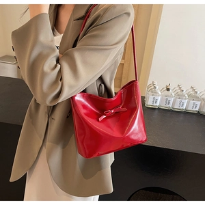 Detail of red glossy shoulder bag featuring a decorative bow and minimalist PU leather texture
