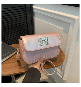 Detail of pink crossbody bag featuring a silver metal bow and glitter texture