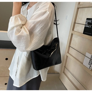 Detail of black patent leather underarm bag with decorative bow and mirror finish