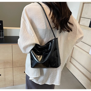 Detail of black patent leather underarm bag featuring a stylish glossy finish and bow