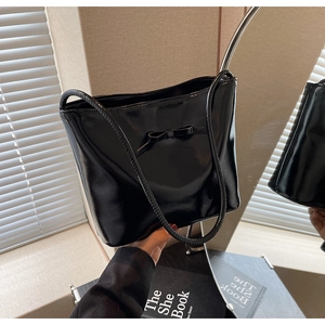 Detail of a black glossy bucket bag featuring a delicate bow and long cylindrical handle