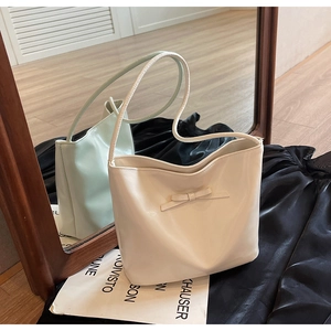 Detail view of cream underarm bucket bag with decorative bow and smooth matte texture