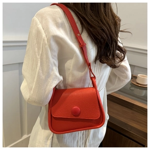 Detail of red pebbled leather crossbody bag with a round buckle worn by a model