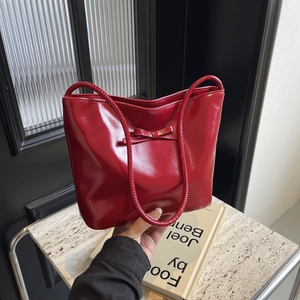 Red patent leather shoulder bag with bow detail shown in a stylish lifestyle setting